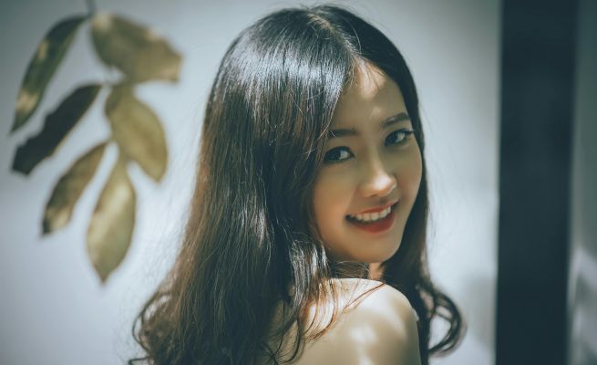 Portrait of a beautiful Asian woman with long hair smiling warmly, captured in an elegant studio setting.